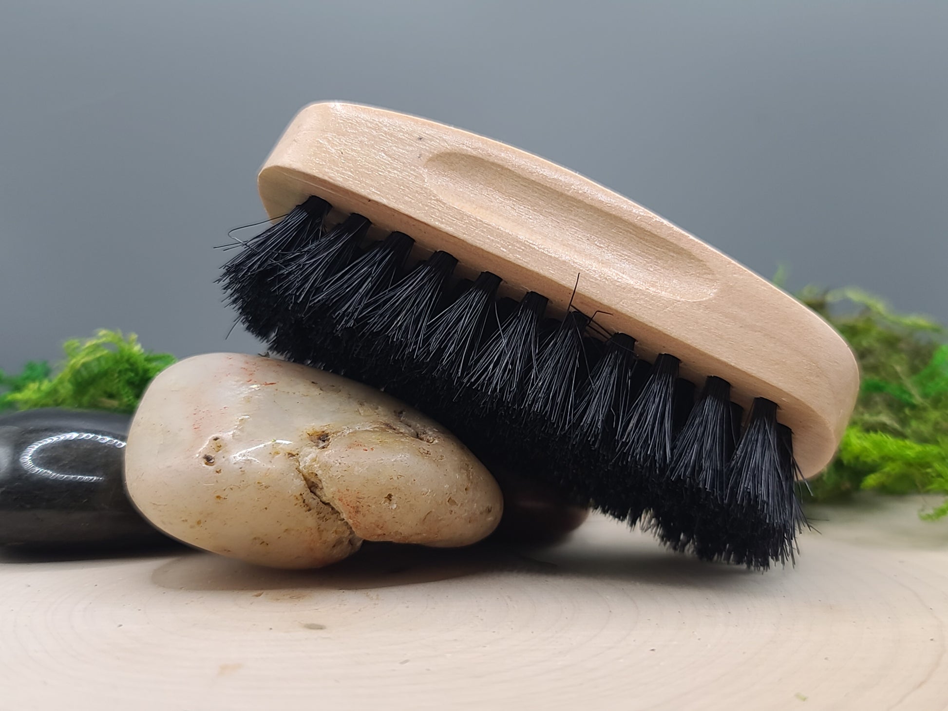 brush with black bristles on a wooden handle, placed on a rock with a natural background.