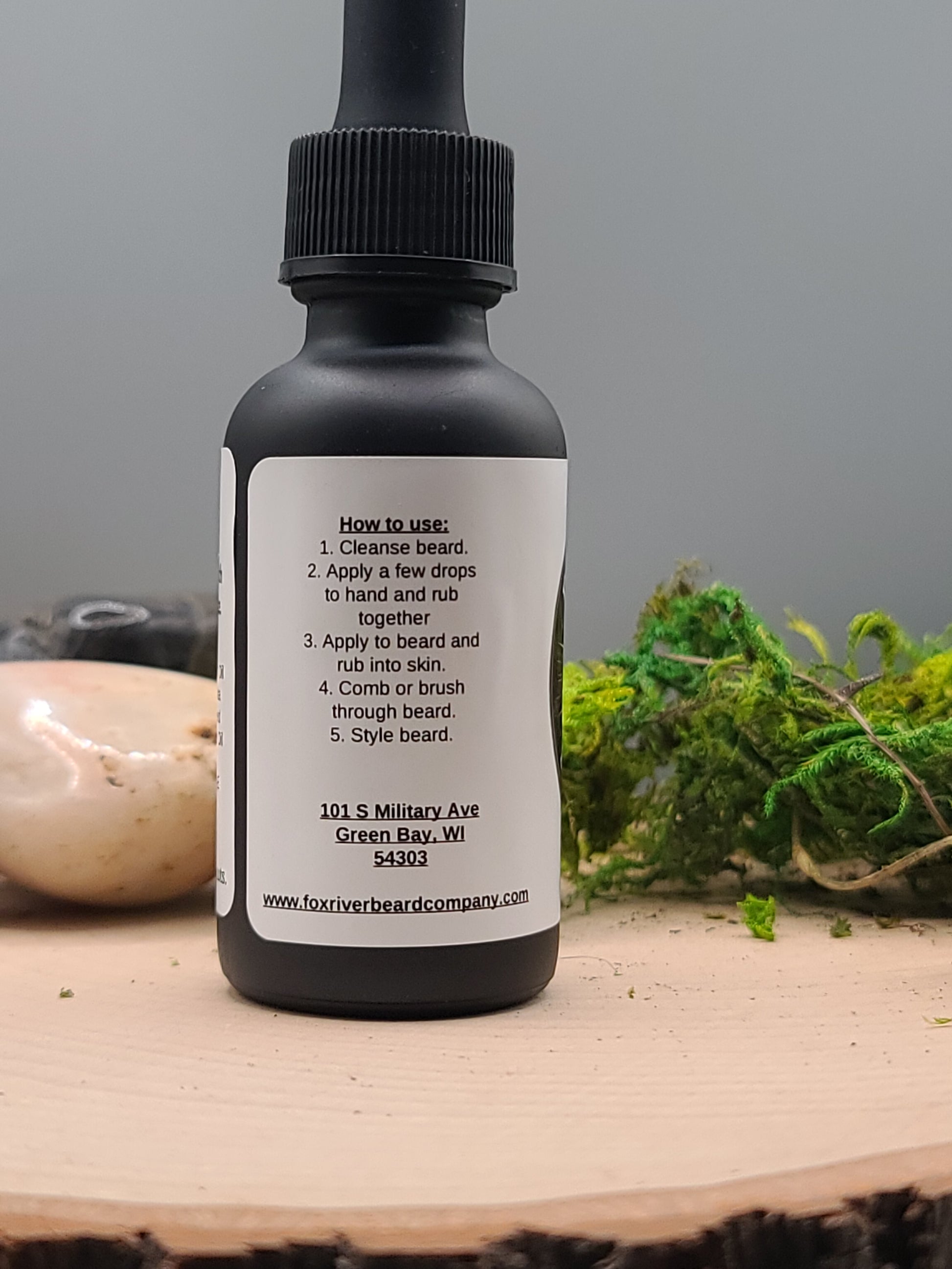 Black bottle with dropper on a wooden surface with greenery